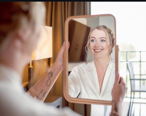 Braut schaut lächelnd in den Spiegel beim Getting Ready in Mettmann