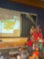 “Elementary teachers dancing in a holiday-themed school assembly with indoor snowfall and live music”
