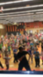 “DJ Reggie leading a Respect Through Hip Hop school assembly with students participating in dance and character lessons”