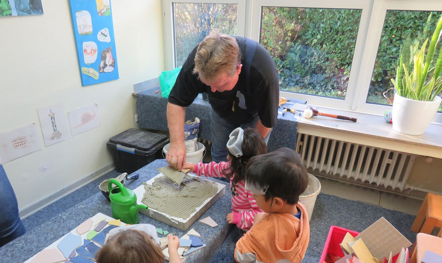 Ein Kindergarten und ein Wohnheim für demente Senioren, die örtlich direkt nebeneinander liegen, wünschten sich, dass die Generationen, welche Corona bedingt lange getrennt waren, wieder zusammenkommen.
In einer im Kindergarten aufgebauten 'Mosaikwerkstatt' gestalten die Kinder unter Anleitung von Robert Kaller Mosaikpflastersteine, die später vom Kindergarten zum Seniorenwohnheim verlegt werden.