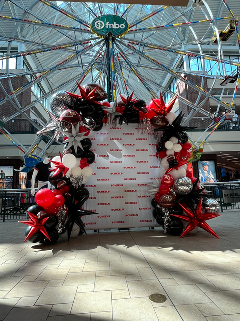 Photo backdrop with a red and black balloon arch inside of a large Scheels sporting good store