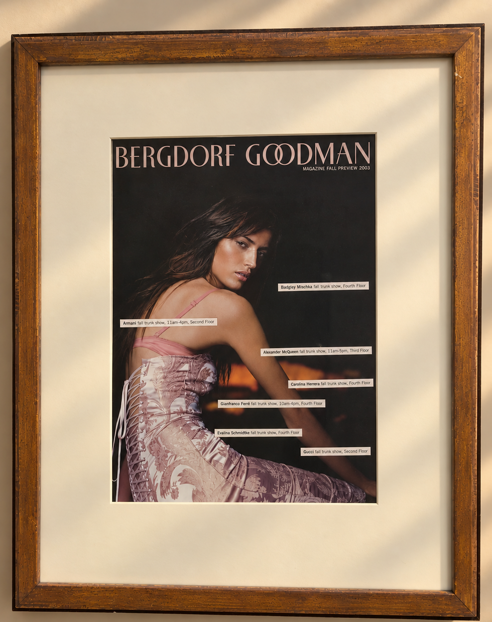 A framed magazine page from the Bergdorf Goodman fall 2003 catalogue with overlayed cut-out names of designers placed on top of the promotional image of a beautiful model wearing a pink damask lace-up the back dress.