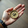 A white man's hand holding a gold compass