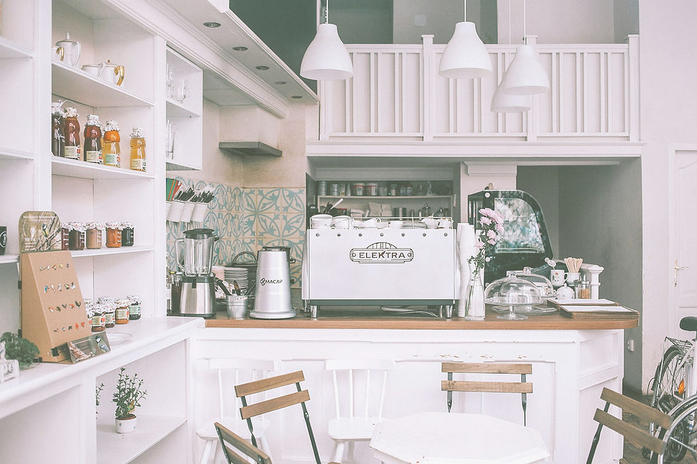 Cozy cafe interior with white decor, light wood chairs, and a counter featuring a white Elektra coffee machine. Warm and inviting ambiance. faith-based family decision. A quiet café breakfast symbolizing a pivotal conversation about faith and family decisions.