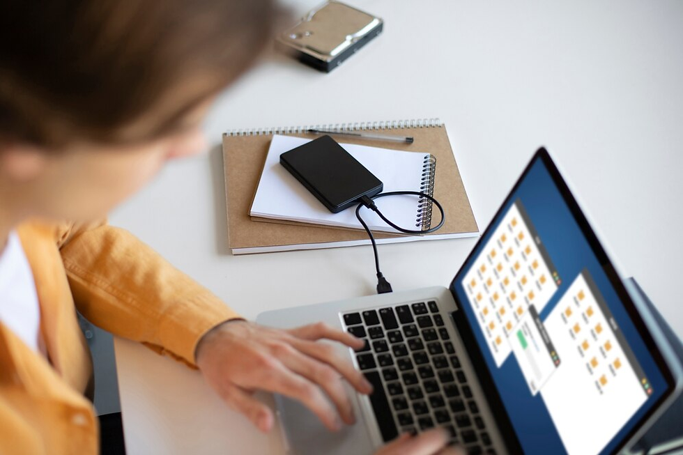 A person using a laptop with external storage attached, managing files on the screen while sitting at a desk.