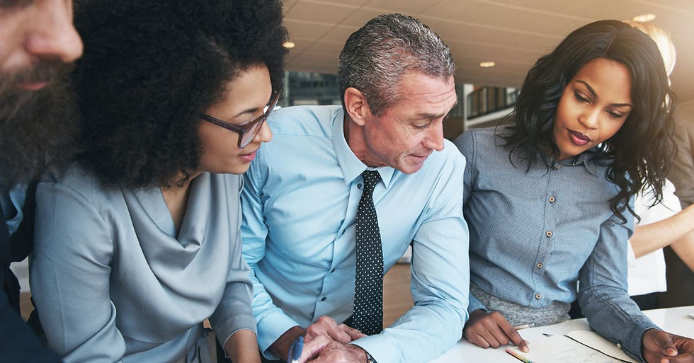 Four people in business attire collaborate over documents in an office. Focused expressions, modern setting, bright lighting.
