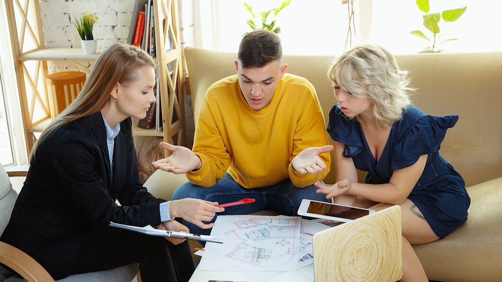 Three people discuss plans on a coffee table in a cozy room. One points at papers, others gesturing. Warm lighting, plants, and books visible.