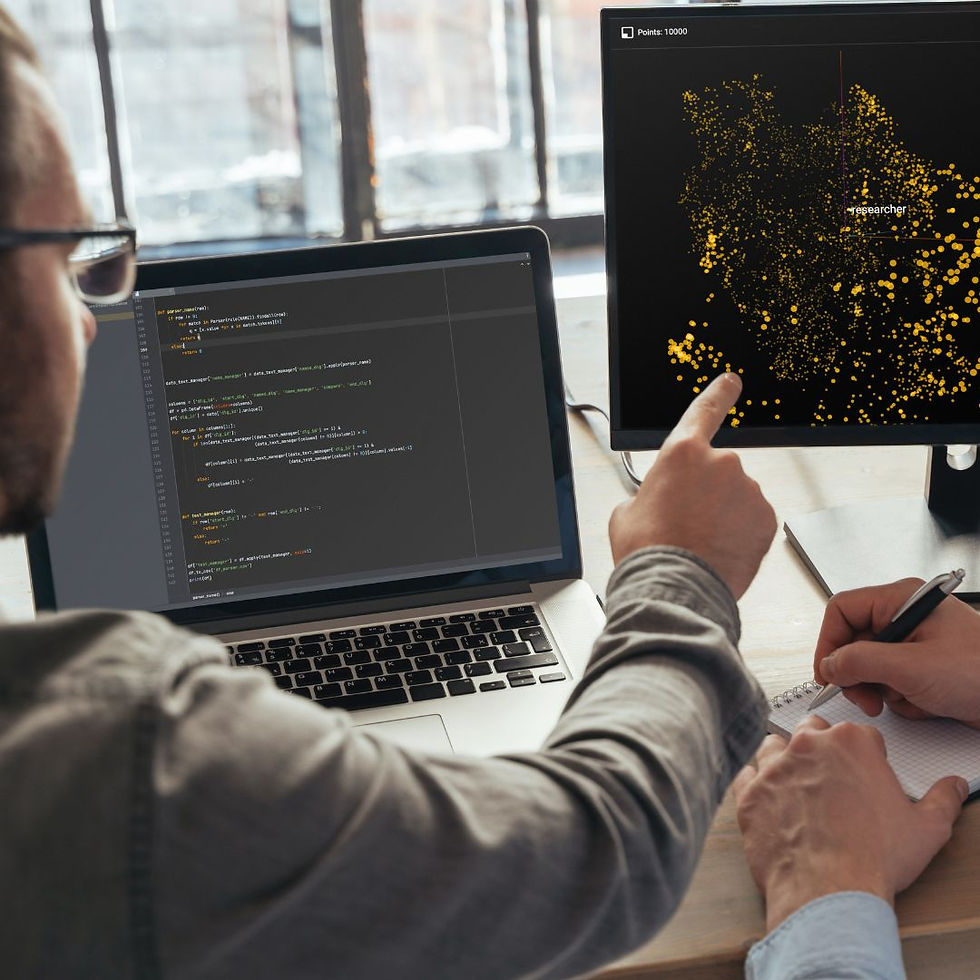 Two people work at a desk with laptops; one points at a monitor showing a yellow data visualization. Coding text visible. Collaborative mood.