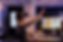 Woman in VR headset interacts with virtual screen in dark office, graphs visible on monitor. Desk has keyboard, papers, and a mug.