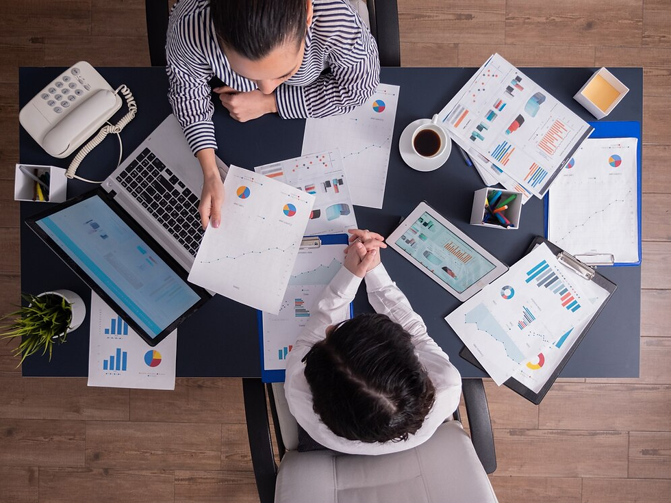 Overhead shot of two professionals reviewing business reports, charts, and graphs at a desk with laptops and coffee.