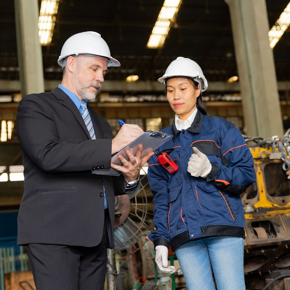Engineer in a suit and worker in a jacket, both wearing helmets, review clipboard in an industrial setting. Focused mood.