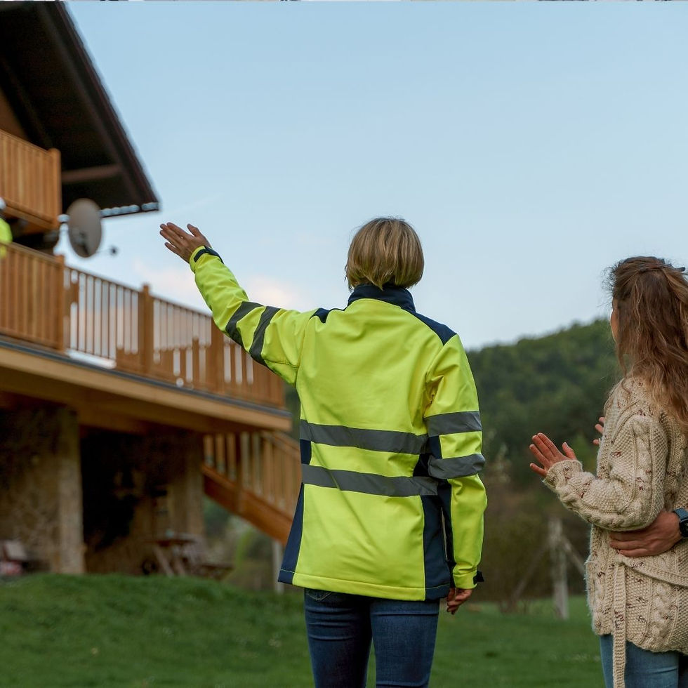 A person in a neon safety jacket points at a wooden house, while another in a sweater observes, set in a lush, hilly landscape.