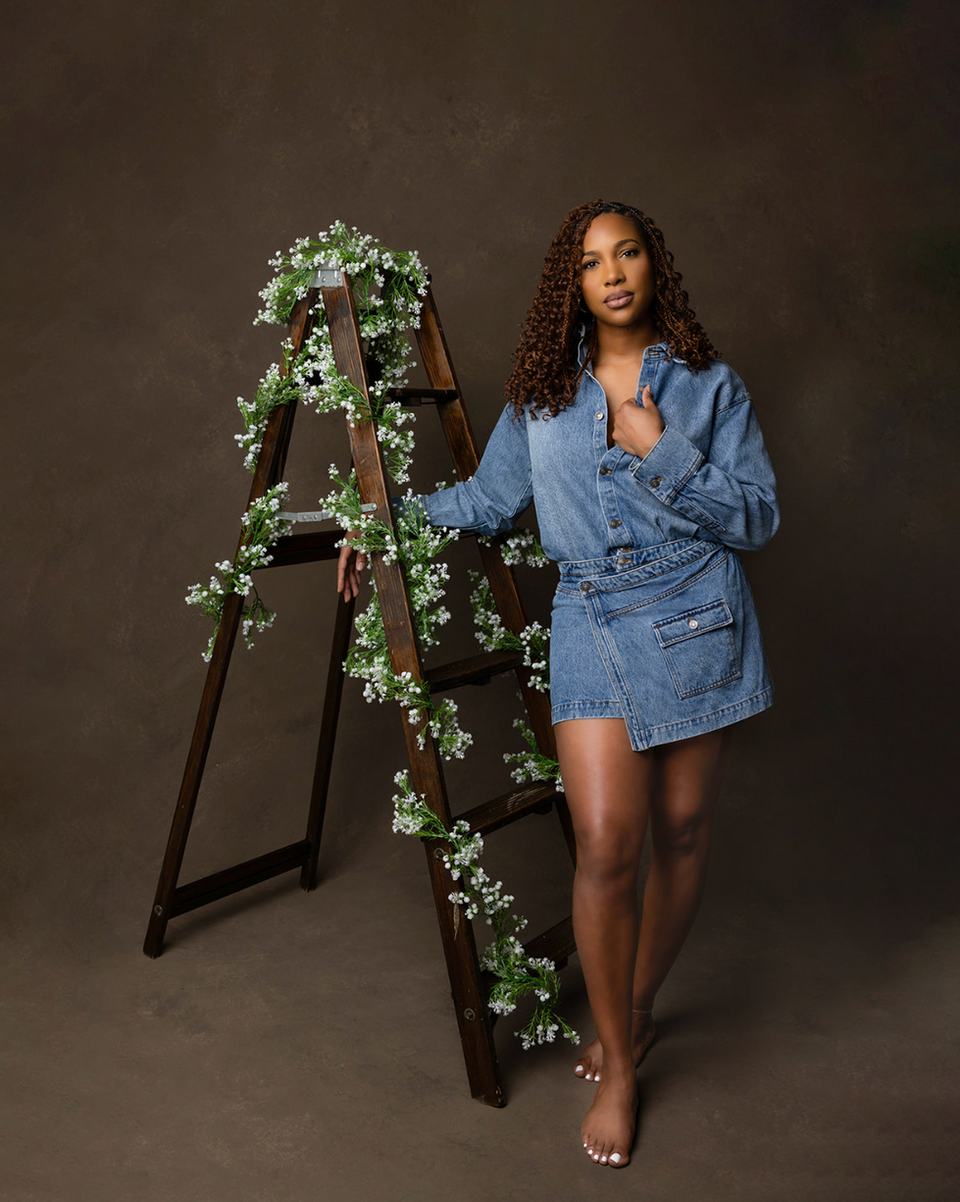 Woman in denim dress standing next to a ladder with white flowers