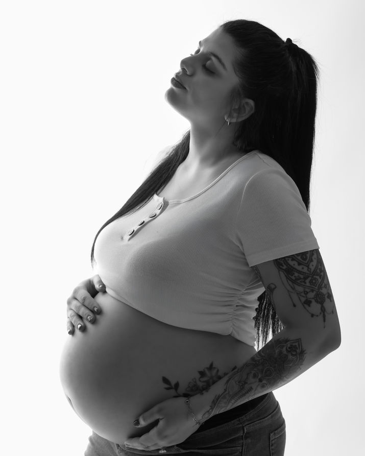 Pregnant woman with tattoos cradling her belly, eyes closed