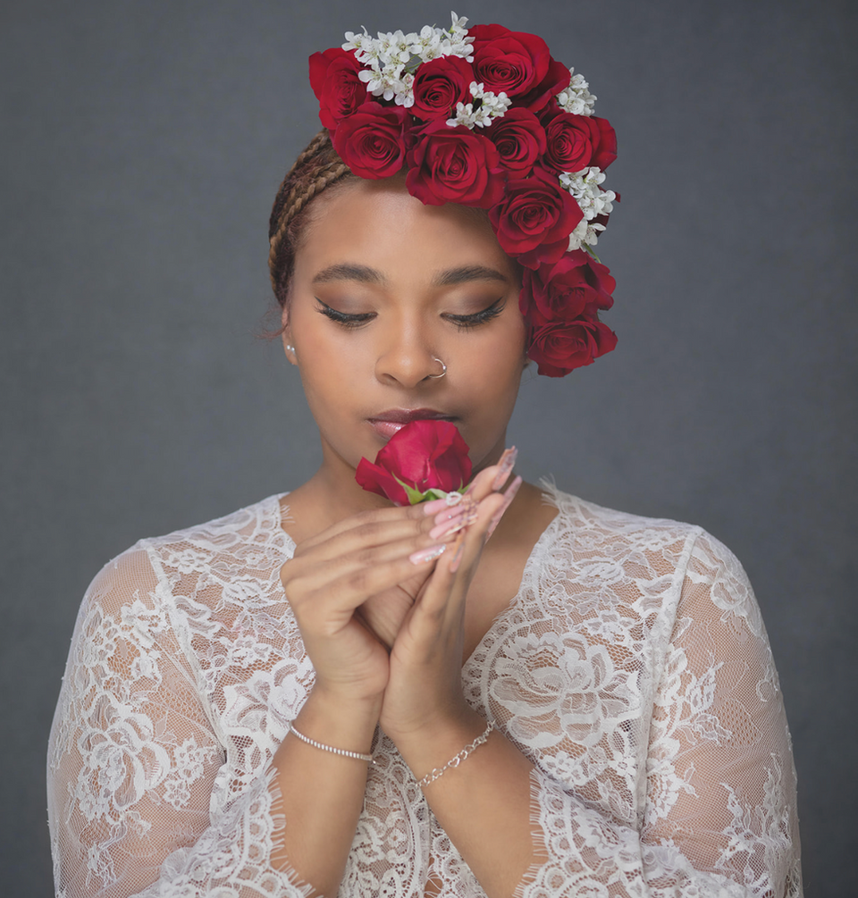 Woman with red rose crown holding a rose to her face