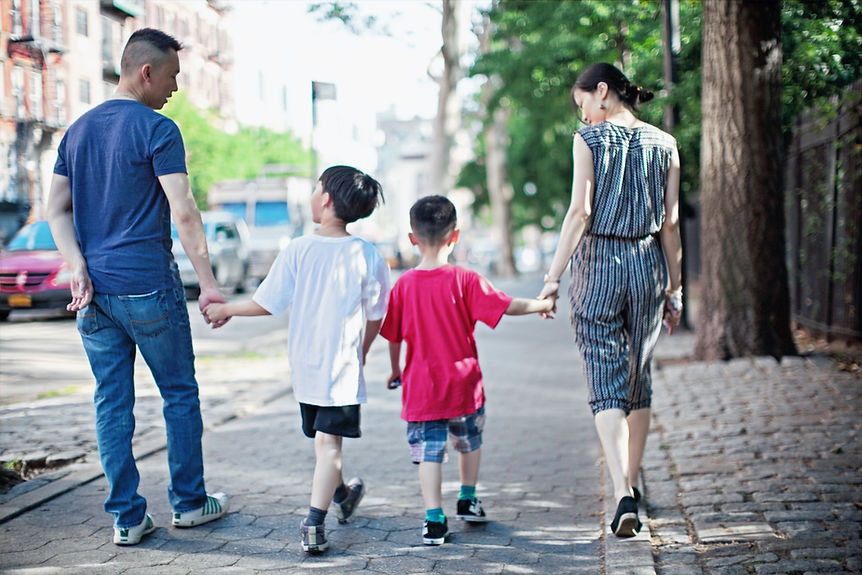 An Asian family of four -- a father, two sons, and a mother -- stand in a line holding hands.