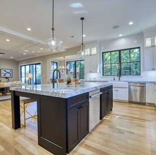 Black kitchen island with quartz counters in white cabinet kitchen.