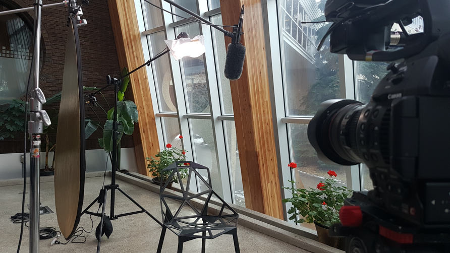 An interview setup of lights, camera, and microphone, with an empty chair in an atrium building
