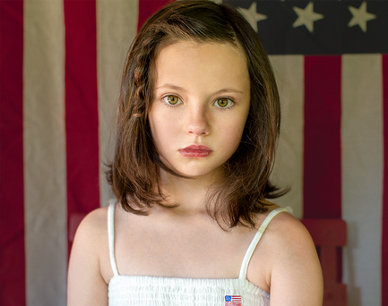 Little girl, somber, American flag background.