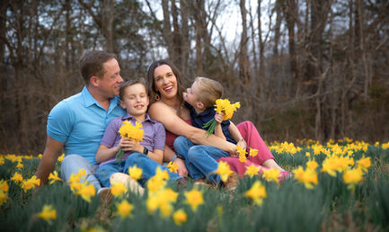 Family sitting and laughing in a field of yellow flowers.