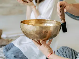 A person holding the bowl and with a stick and practicing holistic techniques 