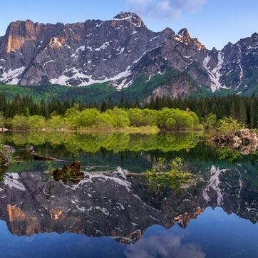 Lago di Fusine con le montagne riflesse nell'acqua e il Monte Mangart sullo sfondo