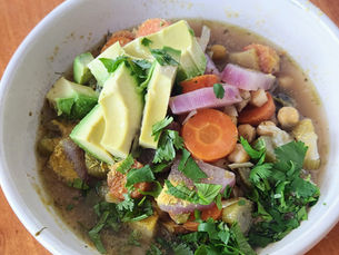 A bowl of Ayurvedic root vegetable soup with chickpeas, carrots, cabbage, and radish in chicken bone broth, topped with fresh cilantro and sliced avocado.