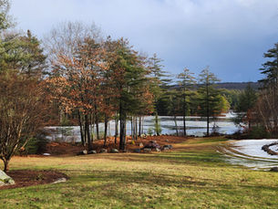 Early spring landscape with melting snow, evergreen trees, and a pond, symbolizing the seasonal transition from winter to spring in nature.