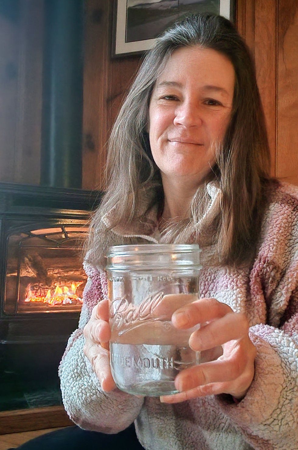 Jennifer holding warm water beside a fire, symbolizing rest, warmth, and soothing respiratory support.