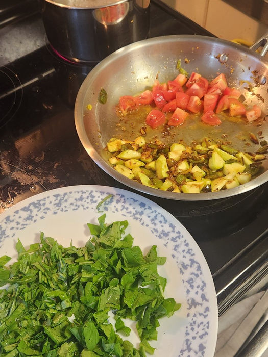 Chopped arugula on a plate beside a skillet of summer squash, pepper and tomatoes as an egg cooks