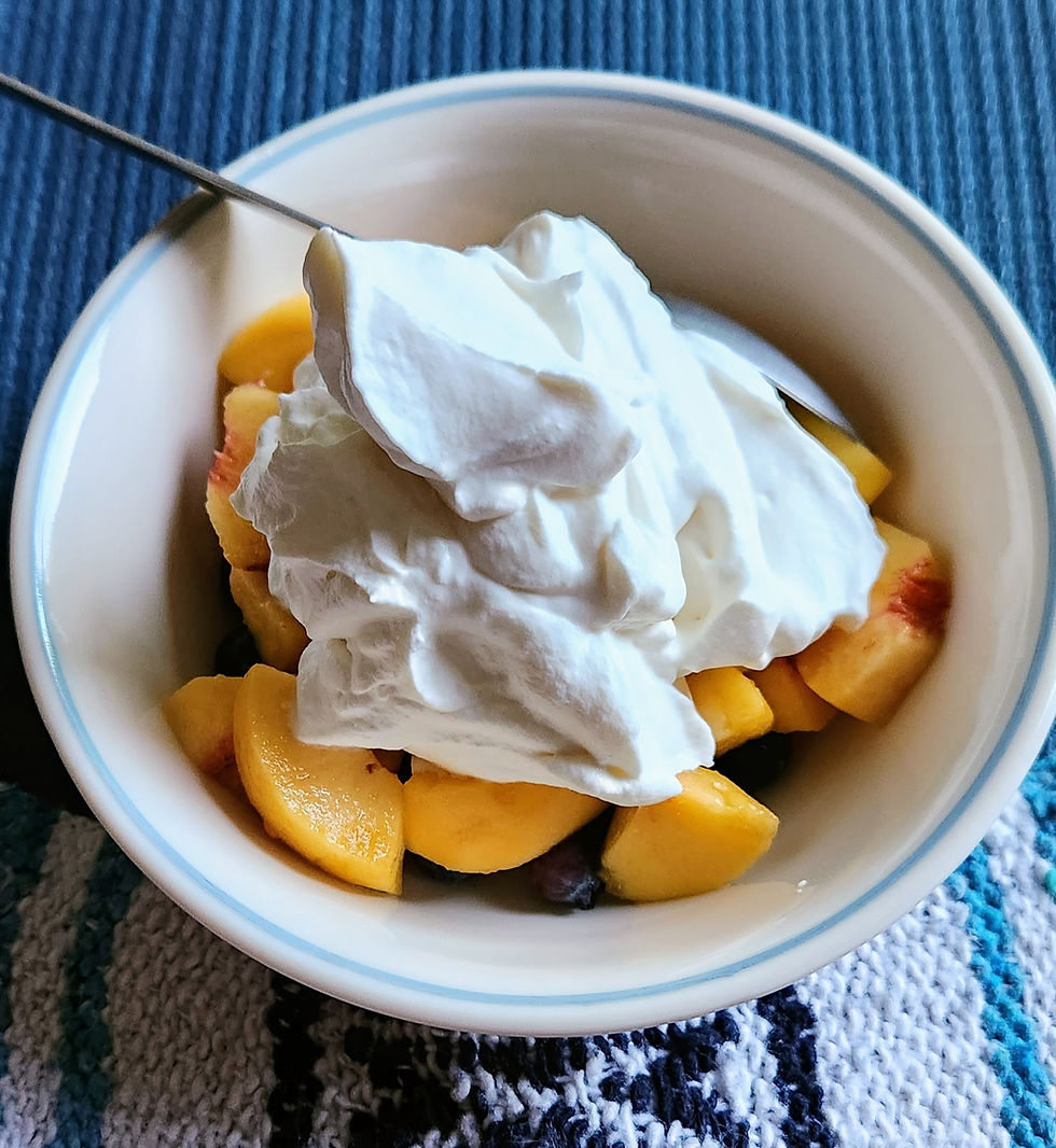 Bowl of fresh peach slices and blueberries topped with creamy yogurt on a blue mat.