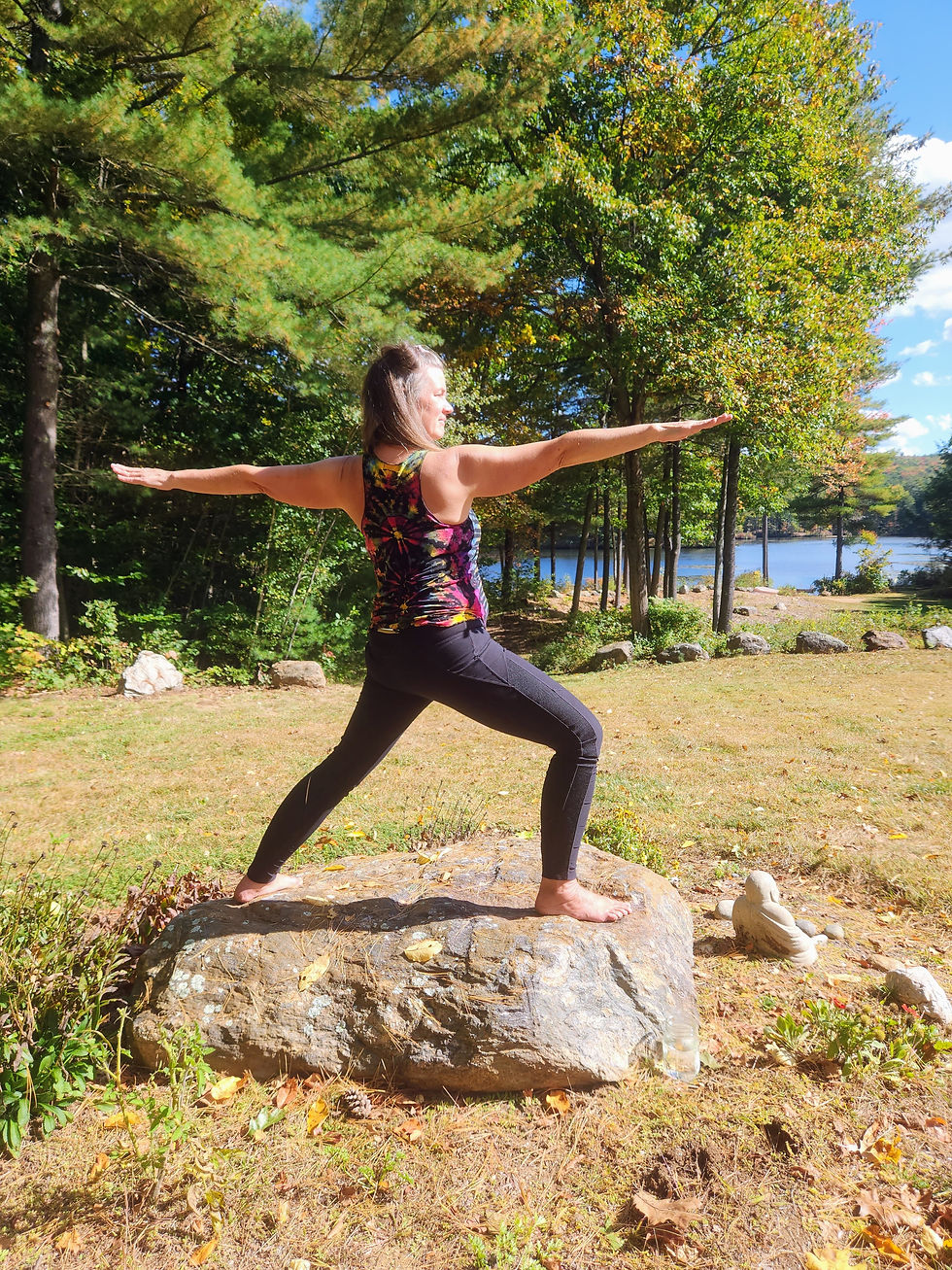 Jennifer practicing Warrior II on a large outdoor rock, demonstrating hip-strengthening alignment to support gluteal tendinopathy during menopause.