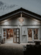 Beleuchtetes Holzgebäude bei Dämmerung mit offenen Türen und gepflastertem Vorplatz.