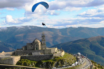 Paraglider boven het berglandschap van Basto in Portugal met uitzicht op groene valleien en heuvels onder blauwe lucht.