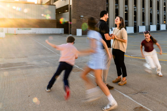 Children running and playing around their parents during a candid urban family photography session at golden hour