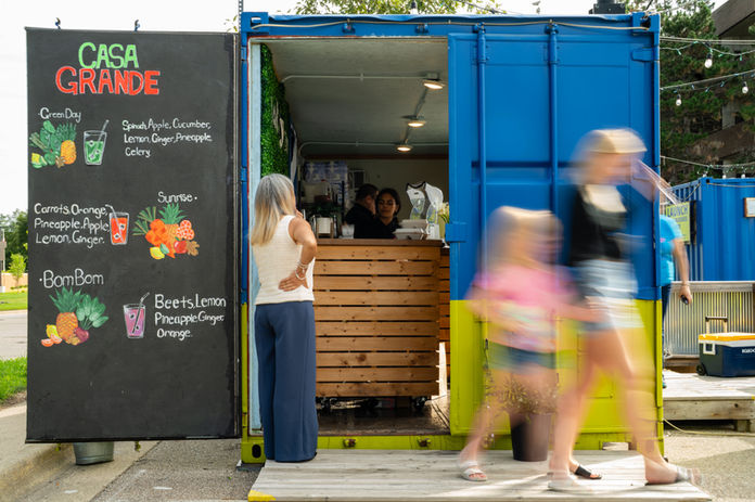 Customers walk past a colorful blue and yellow Casa Grande food stand in Michigan, with motion blur capturing the activity around the business.