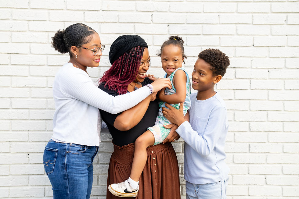 Three women and two children smiling and embracing each other in front of a white brick wall, capturing a joyful family moment.