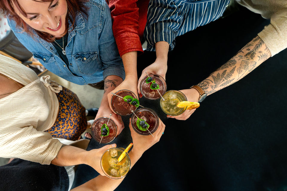 People clinking glasses and sharing small plates at a table, photographed for hospitality brand storytelling.