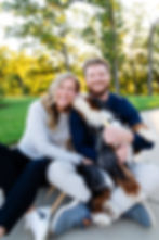 Couple sitting with their Bernedoodle puppy while the puppy is kissing the woman's face at a photography session