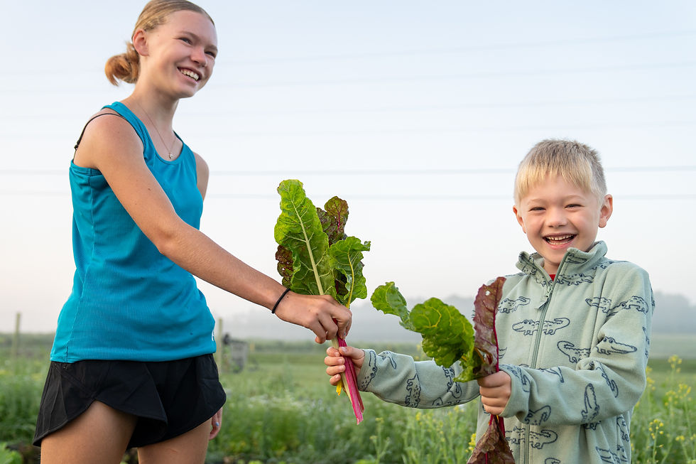 Children smiling and holding freshly harvested Swiss chard at Bankson Lake Farm in Michigan