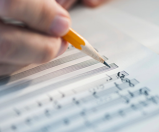 hand holding pencil writing music on manusript paper