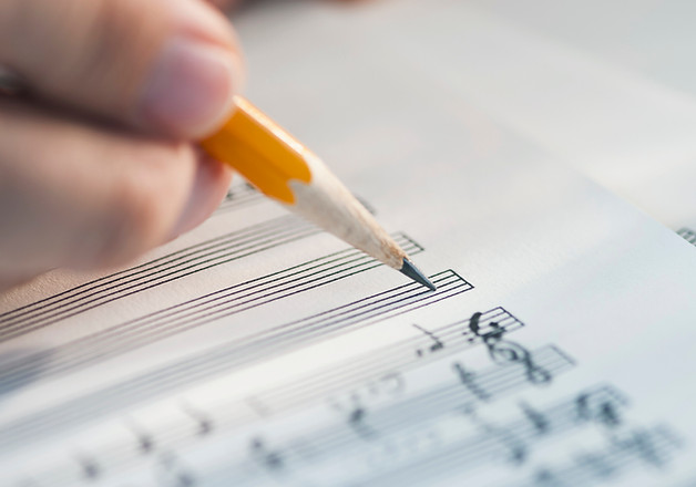 An incomplete sheet of music, a hand holding a pencil, its tip at the beginning of on an empty staff