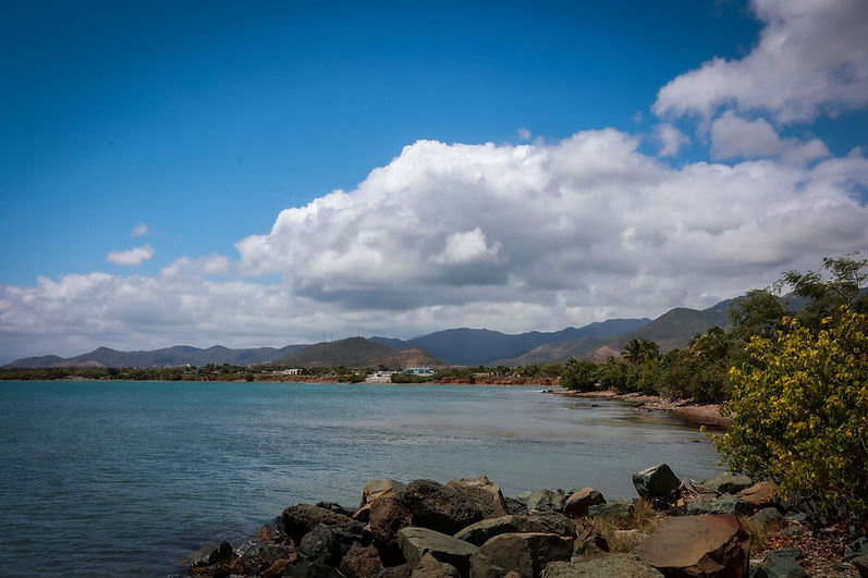 Costa rocosa con mar azul y montañas bajo nubes blancas.