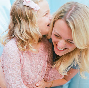 a girl whispers playfully in her mom's ear during a relaxed family photo session with charlottesville photographer Laura Richards
