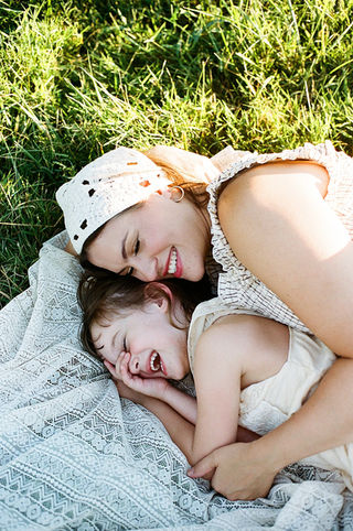a young girl laughing with her mom in the grass during a family photo session at the market at grelen