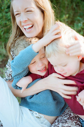 young brothers sit in their mom's lap while she laughs joyfully during a sunrise family session at mcintire park in charlottesville virginia