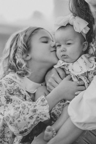 a young girl kissing her baby sister during a sunrise family session at mcintire park in charlottesville virginia