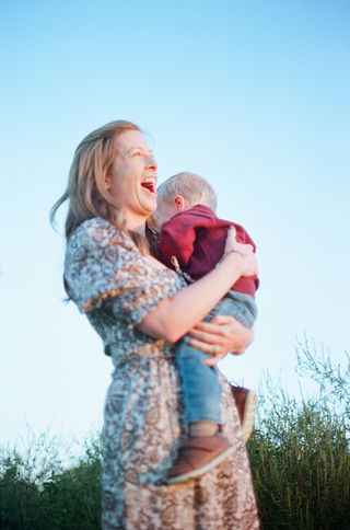 a mom holding her son smiling big and joyfully during a sunrise family photo session at mcintire park in charlottesville