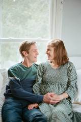 husband and wife look at each other while resting their hands on her pregnant belly