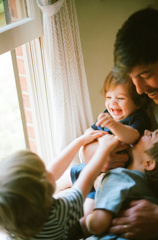 a little boy laughs as his brothers tickle him at their charlottesville virginia home